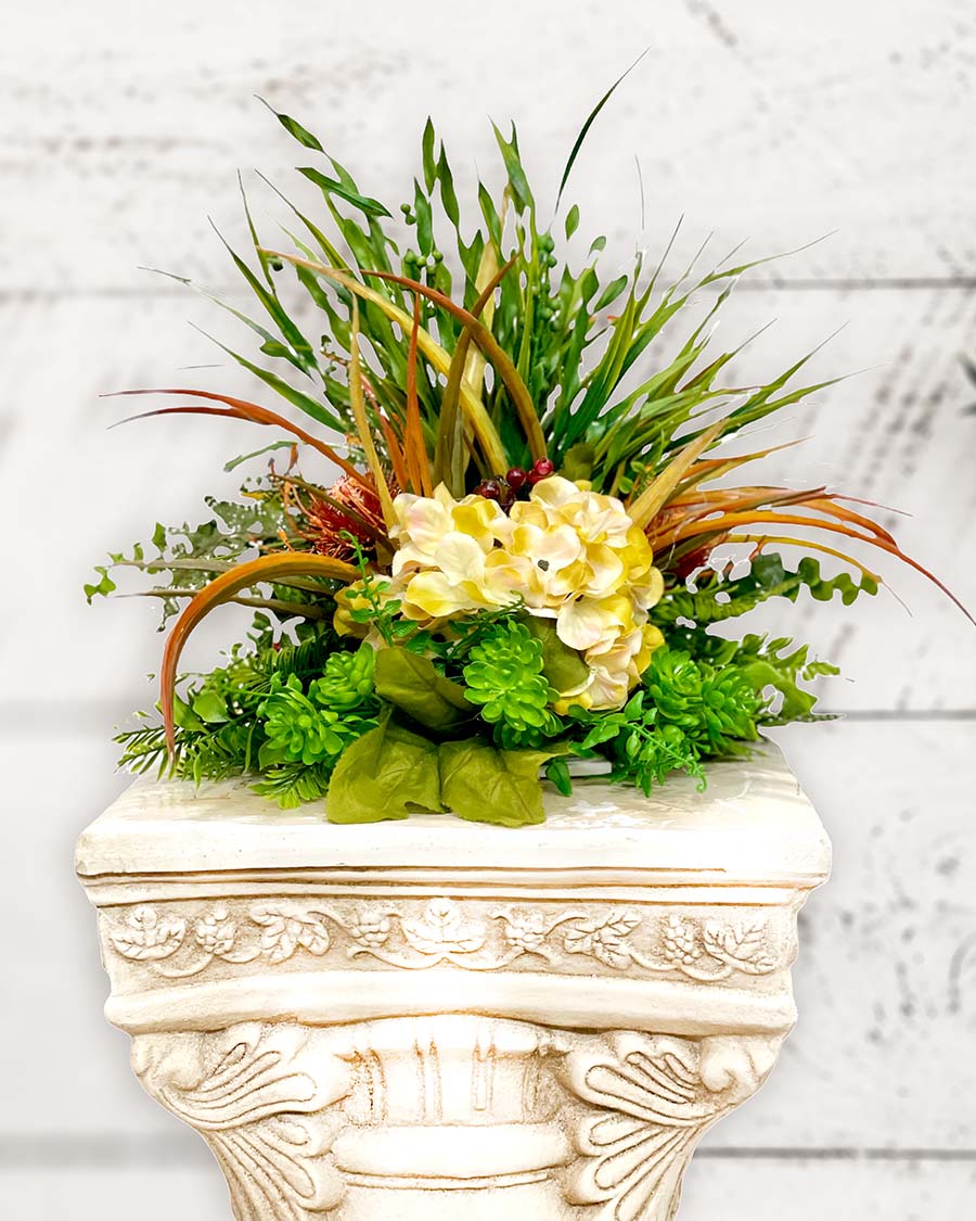 Silk flower sprayed with long leaves and vintage white flowers on a pedestal